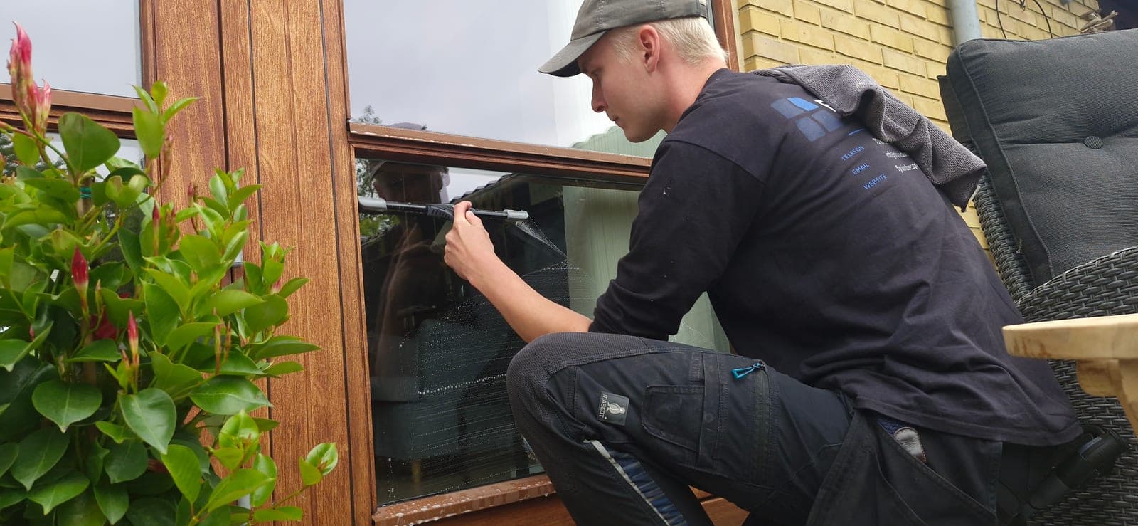 Vinduespudser pudser vindue ved terrasse med skraber hos privatkunde på Fyn